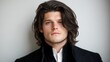 © PaulShlykov - Young man with long hair and blue eyes poses elegantly against a neutral backdrop in a stylish outfit
