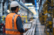 © Alberto Gonzalez  - Engineer in safety vest and hard hat working on a laptop in a modern industrial factory setting.