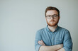 © ZaheerUDin - Portrait of a serious male entrepreneur in a casual outfit with glasses and short hair, standing confidently with arms crossed against a white background, exuding professionalism and determination.
