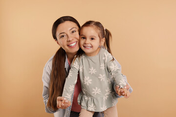 Wall Mural - Portrait of happy mother and her cute little daughter on beige background