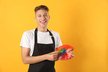 Wall Mural - Smiling man with paintbrush mixing paints on palette against orange background. Space for text