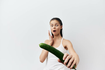 Wall Mural - Surprised woman holding cucumber in a playful pose against a white background, illustrating humor and unexpected reactions in lifestyle imagery Ideal for food and surprise themes