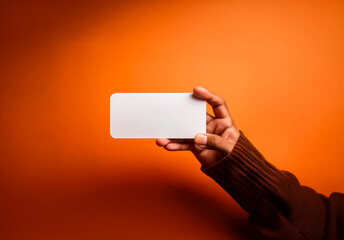 Leinwandbilder - A hand with brown skin holds a blank white card against a bright orange background, presenting a clear, empty space for text or design.