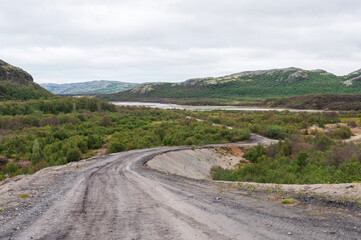 Wall Mural - Winding gravel road leading to the Rybachy Peninsula in Murmansk region, Russia. Titovka River Valley, summer time