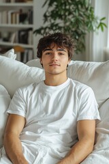 Wall Mural - Young man sits comfortably on a white sofa in a cozy indoor space surrounded by plants and bookshelves in the background