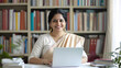 © Mads - A photograph of an Indian woman in her late thirties, smiling as she works on a laptop at her office desk