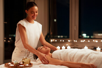 Professional masseuse performing full body massage to young woman client in wellness spa center in tranquil calm candlelit atmosphere