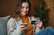 © miss irine - Young happy woman buys online using mobile phone, credit card at home. Female makes fast secure payment. Client shopping, banking, marketing from apartment.