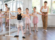 © JackF - Group of ballerinas preparing for performance, learning and improving quality of rendering stage. Ballerinas near ballet bare repeat second position with supervision experienced female mentor