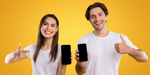 Wall Mural - we like this app. portrait of happy couple holding and showing 2 smart phones with black empty scree