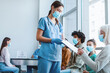 © Prostock-studio - Diverse people waiting in line to get shots or to get tested for flu infection at the hospital. Senior patient signing Informed Consent for Vaccination against pneumonia, influenza or coronavirus