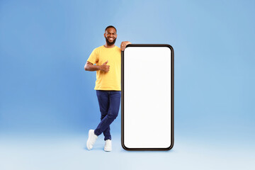 Wall Mural - new mobile application. handsome young african american guy standing near big cellphone with empty s