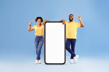 Wall Mural - positive african american couple demonstrating huge smartphone, offering mockup for your app or webs