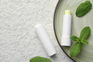 Sticker - Mint lip balms and green leaves on beige textured background, top view. Space for text