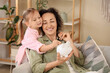 © Pixel-Shot - Little girl with her mother and piggy bank at home