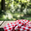 © Gustav - A Rustic Picnic Setup, Red and White Gingham Cloth on Weathered Wooden Table with a Blurry Verdant Forest Backdrop suggesting Tranquility