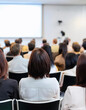 © lina - rear view of a large audience attentively listening to a presentation in a conference room