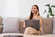 © PRIME STOCK LAB - Woman sitting on sofa with laptop, smiling while using wireless earbuds in bright living room.