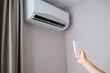 © GRON777 - Woman holding air conditioner remote control and setting cooling temperature on split system to 17 degrees, in hotel room, at home. Concept of air cooling in hot room, climate control at home