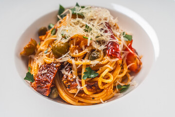 Wall Mural - Spaghetti or Putanessa pasta according to a traditional Italian recipe with anchovies, olives, capers and tomatoes on a white plate. Close-up. Space for text.