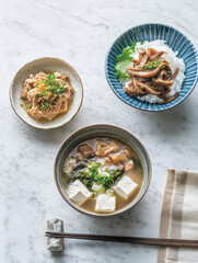 A comforting Japanese miso soup with tofu, mushrooms, and greens, accompanied by a rice bowl with braised mushrooms and a side dish of minced meat.