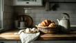 © Hannah - Breakfast still life: Eggs, croissants, and a tea kettle set on a rustic kitchen countertop.