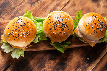 Wall Mural - Three burgers with patty, cheese and lettuce on a wooden board and background. Close-up. Space for text. Top view.