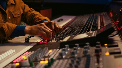 Leinwandbilder - African american producer uses control desk with automatic equalizer, mixer and sliders to edit tracks in post production. Sound engineer processing audio recordings, mixing console. Camera B.