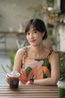 © Jirawatfoto - Asian woman in colorful dress enjoys refreshing iced coffee at outdoor cafe, surrounded by greenery and relaxed atmosphere