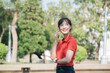 © Jirawatfoto - Asian cheerful young woman in red shirt talking on her phone while standing outdoors in sunny park