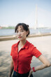 © Jirawatfoto - Asian confident woman in red shirt poses outdoors near river with bridge in background on sunny day