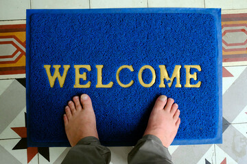 Wall Mural - Door mat with word welcome near entrance, top view. Man at entrance.