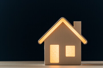 Poster - A cardboard model house on a rough timber plank, backlit by a mellow, honey-toned glow,