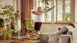 © master1305 - Elderly man in home wear listening to music in headphones and dancing in modern living room at home with potted plants and grey couch. Concept of happiness, elderly lifestyle, relaxation