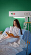 © master1305 - Smiling teen girl sitting in bed, reading book while having drip procedure in modern, well-equipped clinic. Recovery process. Concept of health care, medical treatment
