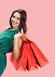 © vgstudio - Portrait image - beautiful brunette hair woman, cute girl wear green dress hold hand red shop bags wile stand on blank empty mockup, free place for ad text isolate rose pink background. Sale concept.