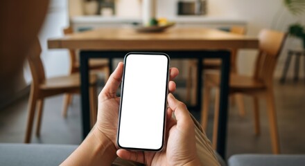 Person holding a smartphone with a blank screen in a cozy interior setting