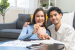 © KMPZZZ - Happy smile asian young couple love hand putting coin in piggy bank for saving money to buy real estate for new home. Business finance, deposit with banking for financial planning future together.