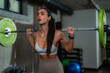 © DusanJelicic - Young woman bodybuilder performing squats with a barbell on her shoulders, exercising her leg muscles in a modern gym, showing strength and determination in her workout