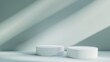 © liliyabatyrova - Soft rays of light illuminate a minimal white podium display, featuring two round cosmetic containers on a smooth surface, creating a tranquil and stylish atmosphere