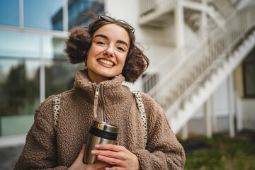 Wall Mural - beautiful young woman hold thermos and stand in front modern building