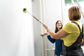 Mother and daughter enjoying together while painting wall.