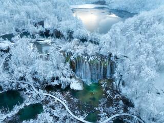 Wall Mural - aerial drone view of frozen lake, waterfall and snowy forest at sunset. winter fairytale in plitvice