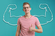 © New Africa - Handsome young man with drawing of strong arms behind him on light blue background
