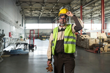 Leinwandbilder - Experienced male worker of factory putting on yellow protective helmet while standing in spacious workshop or plant