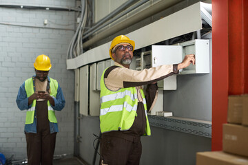 Leinwandbilder - Mature engineer in workwear looking at lamps on ceiling while switching on electricity in plant or warehouse before work
