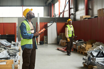 Leinwandbilder - Young African American male engineer in workwear looking upwards and pressing buttons on control pad against colleague