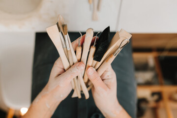 Fototapete - Potter holds craft instruments for clay sculpting. Wooden craft tools for molding ceramic crockery.