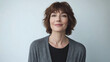 © Infinity Lens - Smiling attractive woman in her late thirties with short brown hair and bangs wearing gray cardigan and black shirt standing against white background.