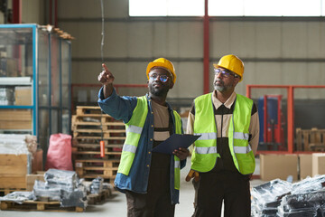 Leinwandbilder - Young man in workwear pointing at new industrial equipment while discussing its quality with mature colleague